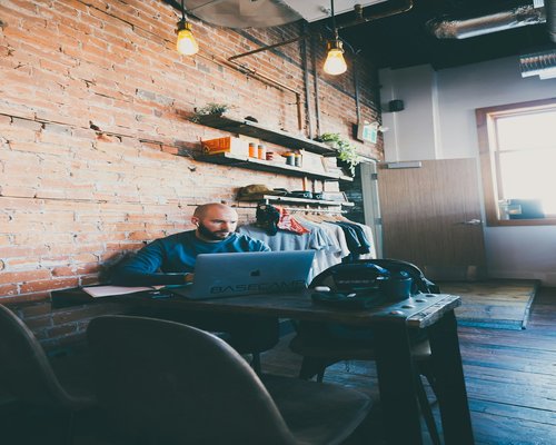 A person typing on a laptop at a rustic wooden table with coffee
